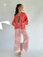Woman wearing a coral jacket and patterned pants against a white background
