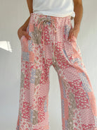 Floral patterned pants worn by a person on a plain background showing elastic waistband and drawstring with hands in pockets