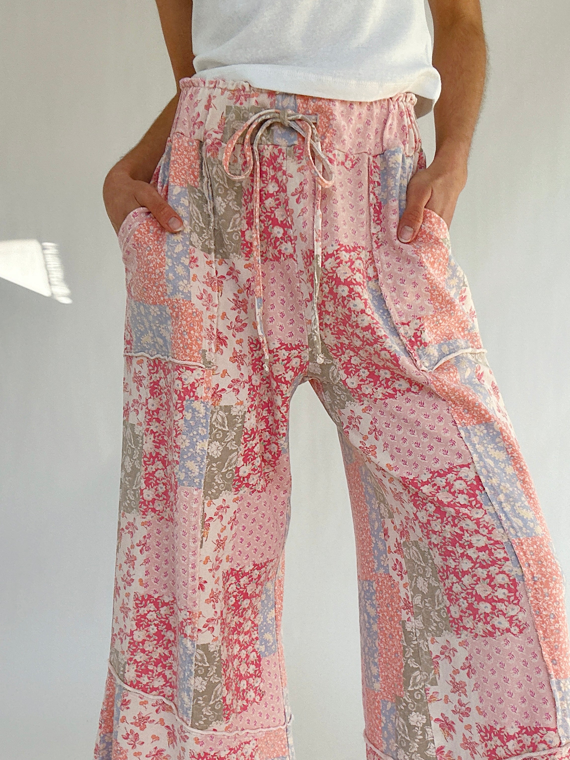 Floral patterned pants worn by a person on a plain background showing elastic waistband and drawstring with hands in pockets