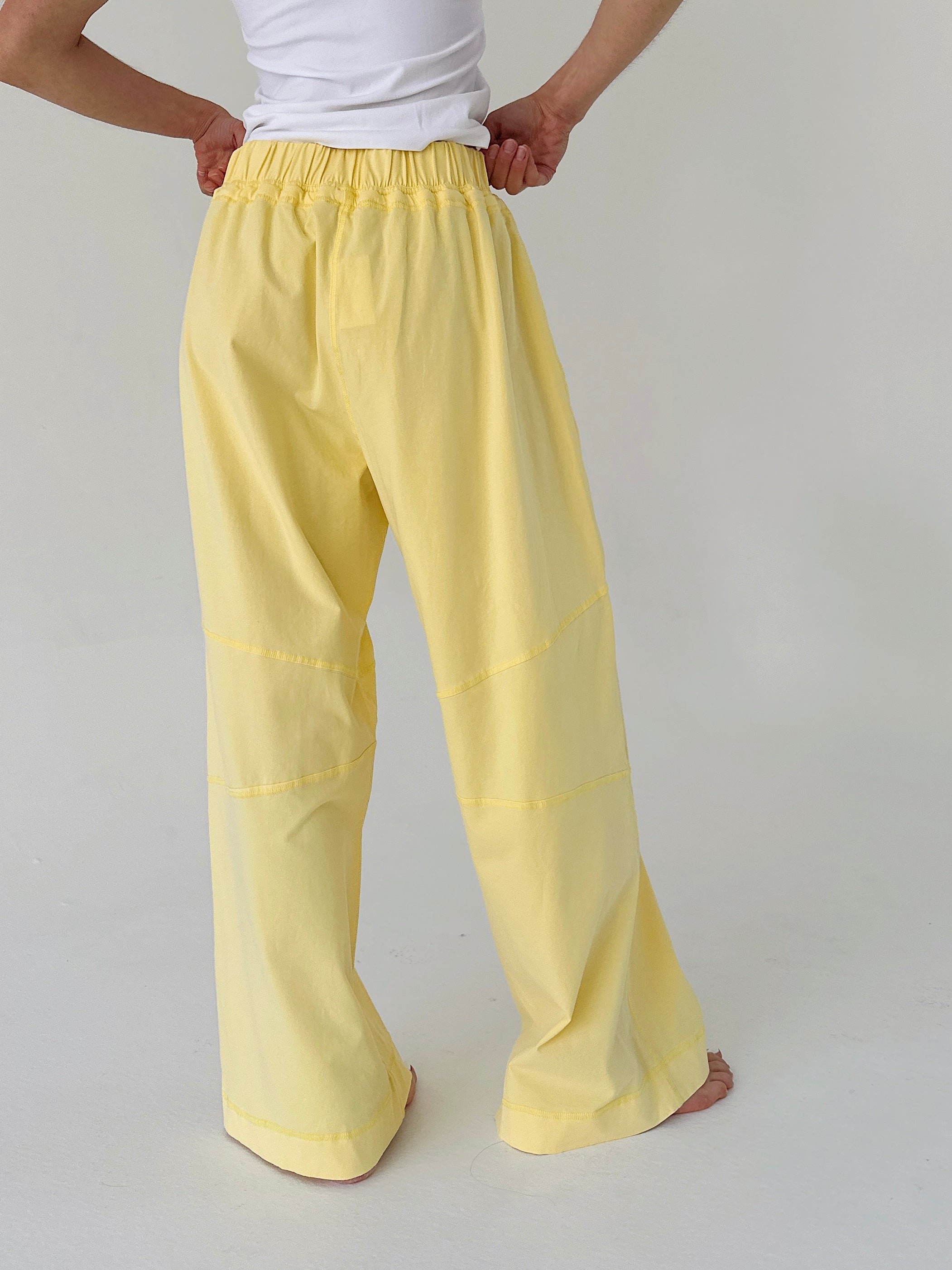 Person wearing yellow pants and a white shirt on a plain background from back