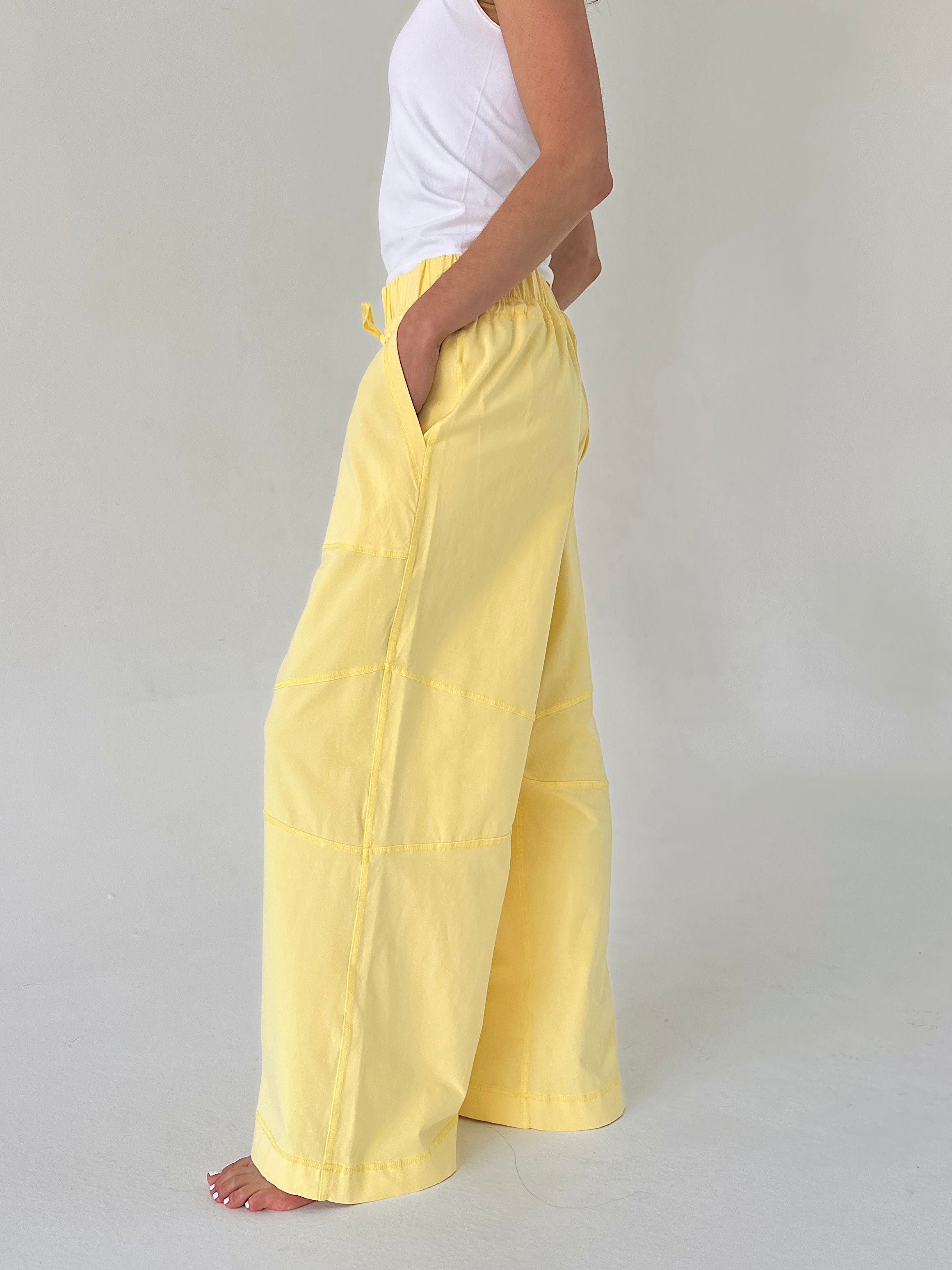 Person wearing yellow pants and a white top on a plain background from side
