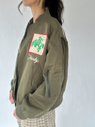 Person wearing a green jacket with a cowboy patch and cargo pocket on a white background