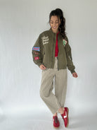 Woman wearing a green jacket with western patches, red shirt, and plaid pants on a white background