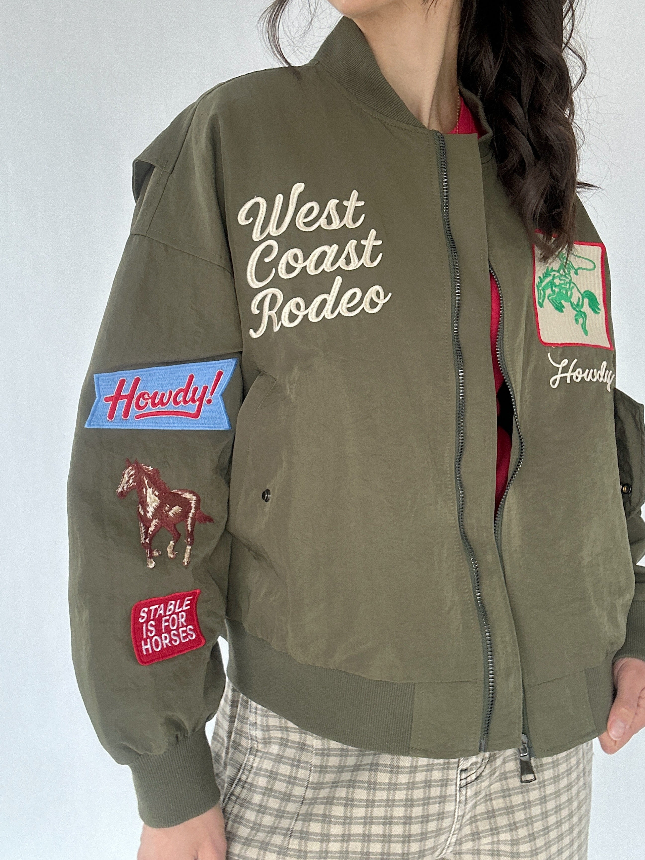 Green bomber jacket with patches and text worn by a person on a white background