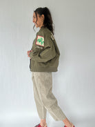 Woman wearing a green jacket with a logo and text, standing against a plain background from side