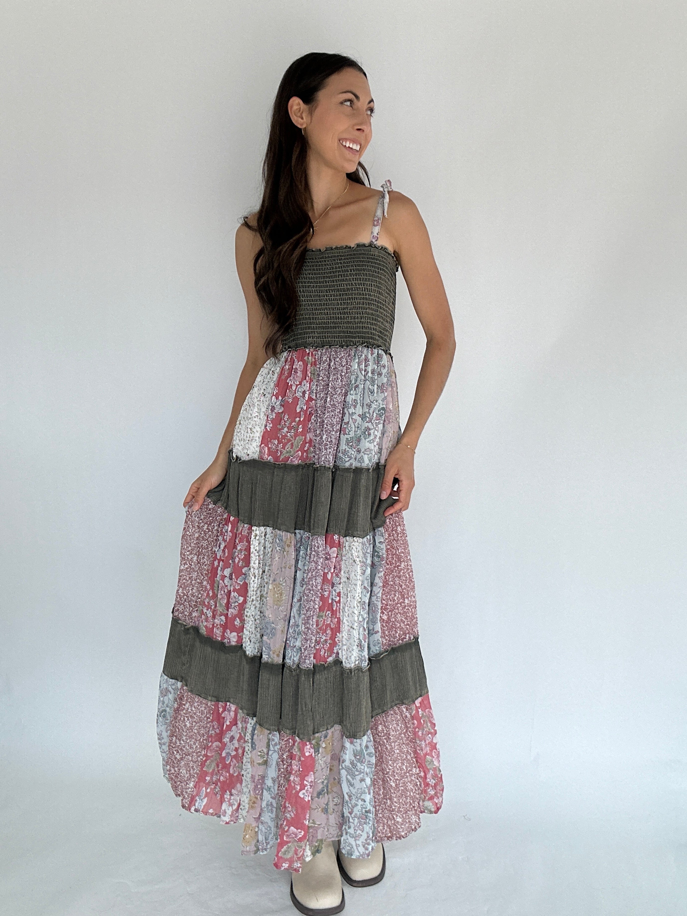 Woman wearing a long, layered dress with a mix of patterns and colors against a plain background.