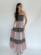 Woman wearing a long, layered dress with a mix of patterns and colors against a plain background.