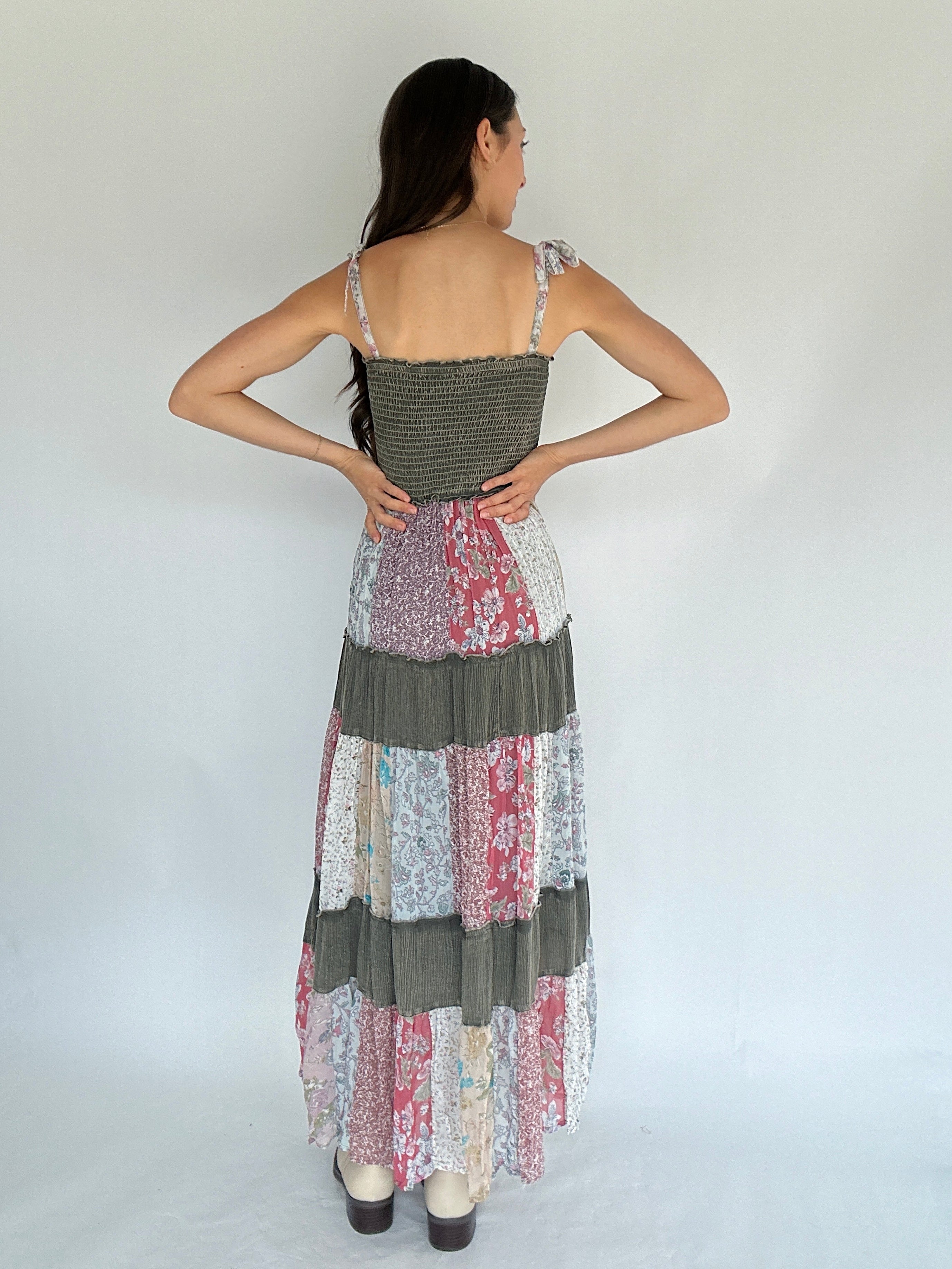 Woman wearing a patchwork dress with floral patterns on a plain background back view showing smocked back