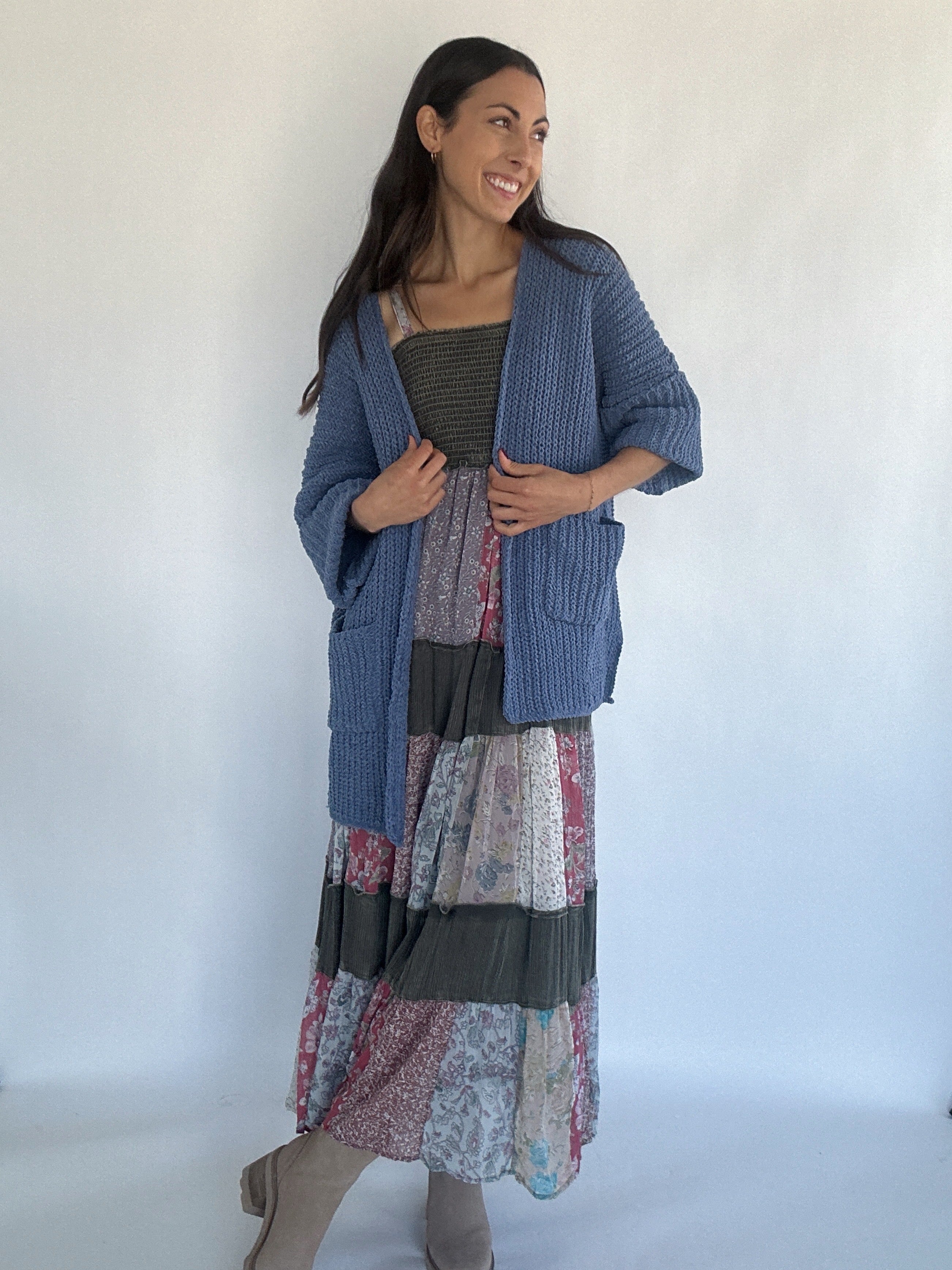 Woman wearing a blue chenille cardigan over a patchwork dress against a white background