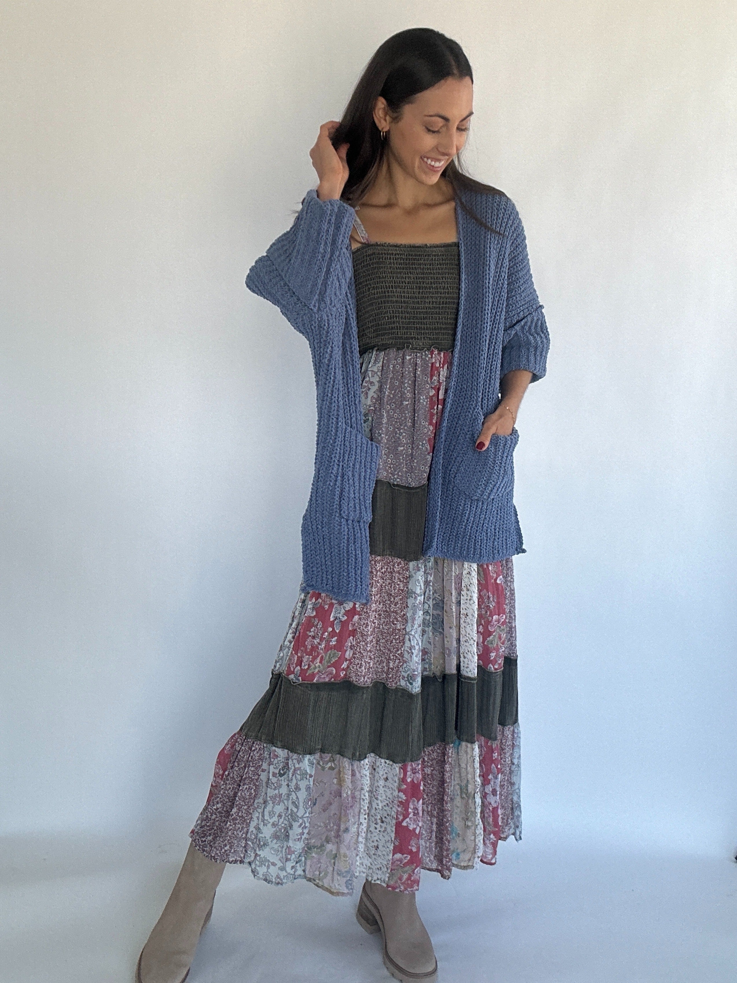 Woman wearing a blue chenille cardigan over a layered patchwork dress with a white background