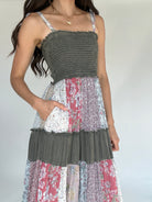 Woman wearing a patchwork dress with floral and solid patterns on a plain background showing smocked top and side pocket
