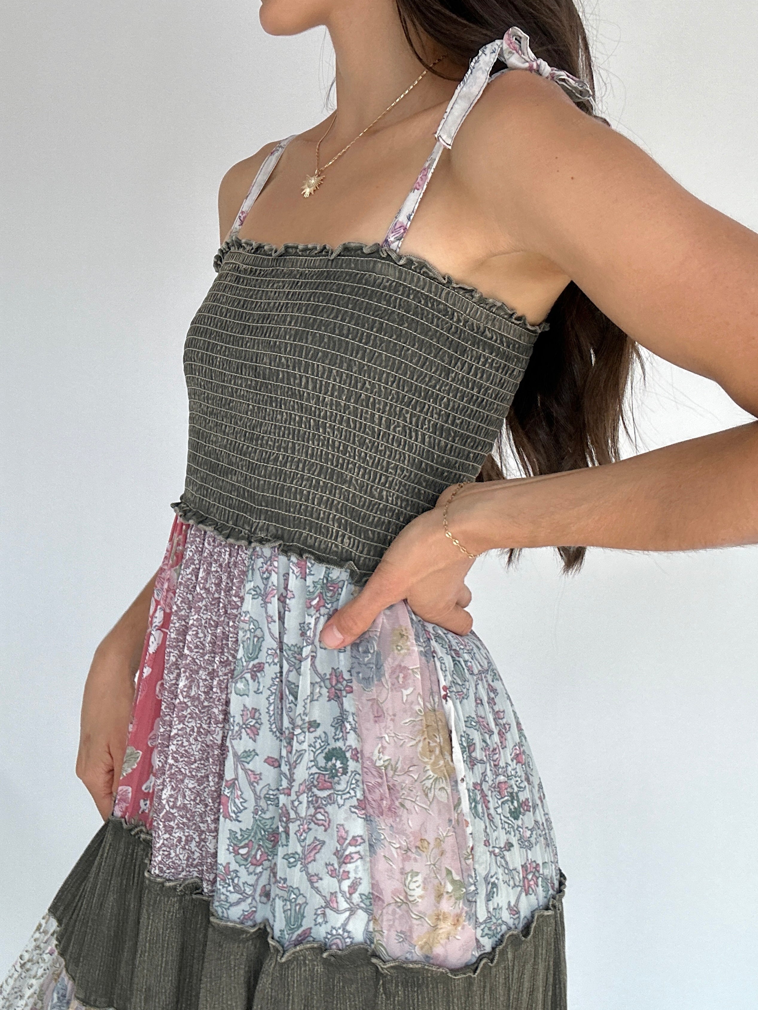 Person wearing a layered dress with a textured smocked top and floral skirt against a white background