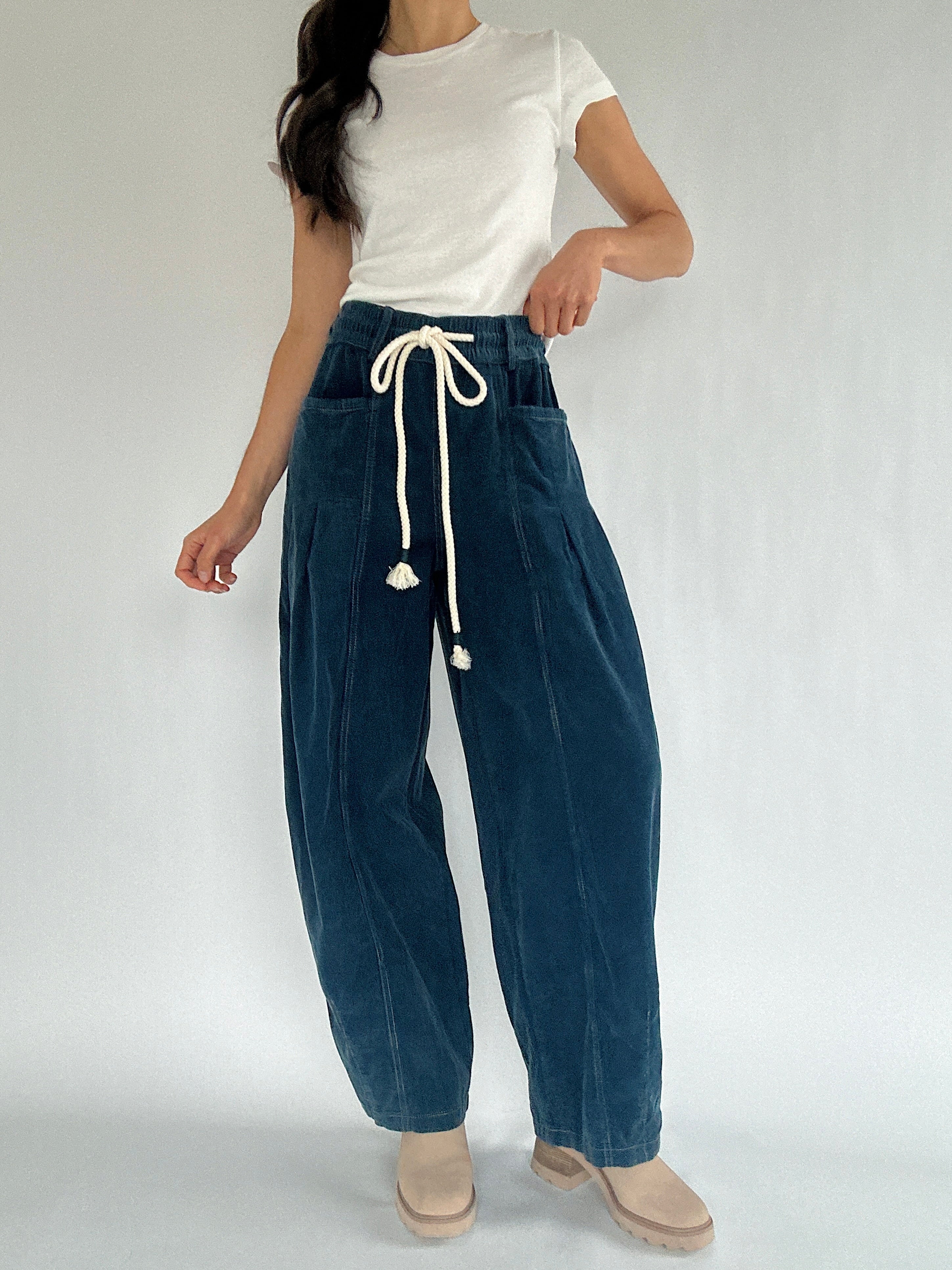Person wearing blue corduroy barrel pants with a white top on a plain background