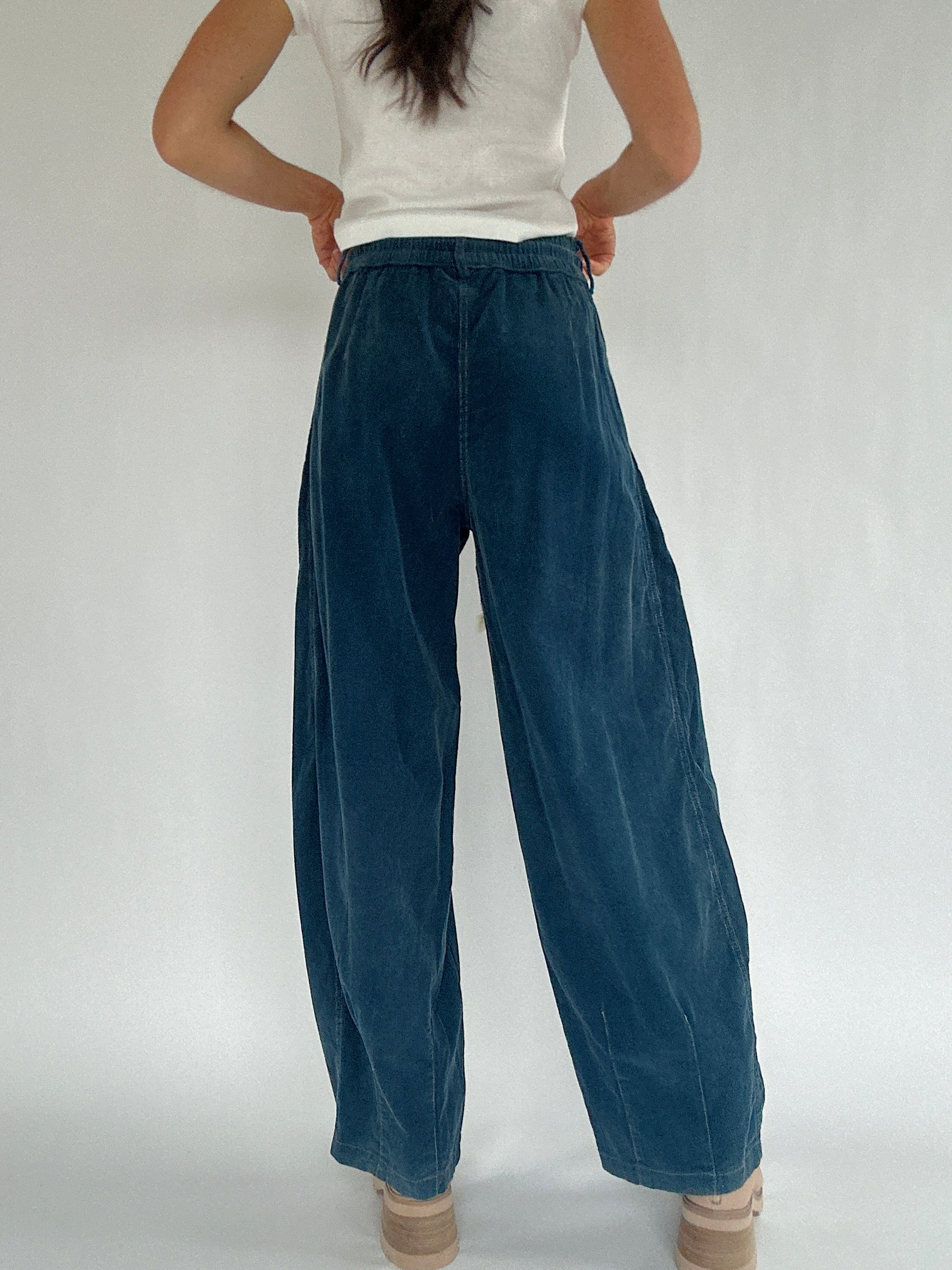 Person wearing blue corduroy wide-leg pants and a white top on a plain background from the back