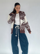 Woman wearing a nordic brown patterned cardigan and blue pants against a white background