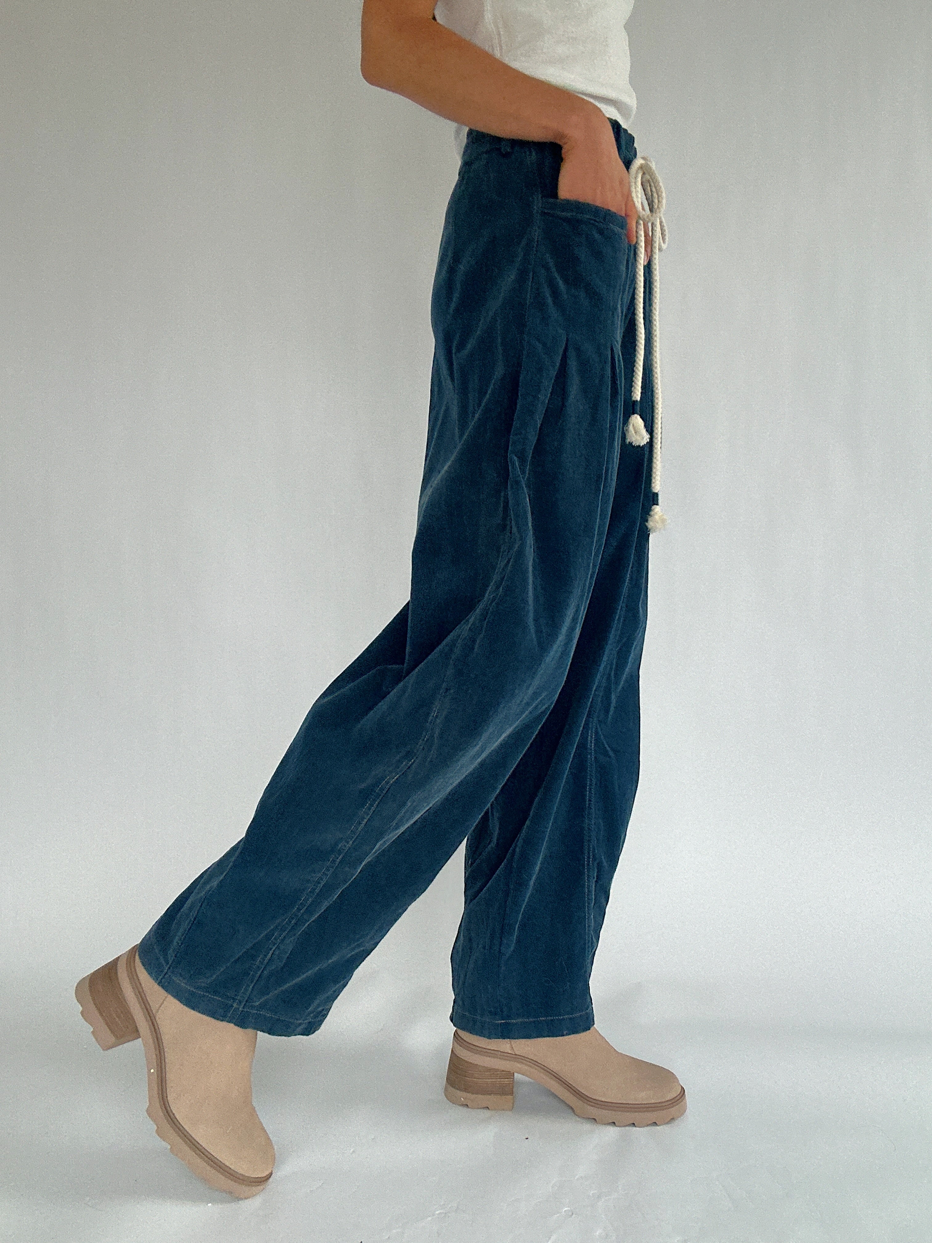 Person wearing blue wide-leg pants with a white background from side and hands in side pocket