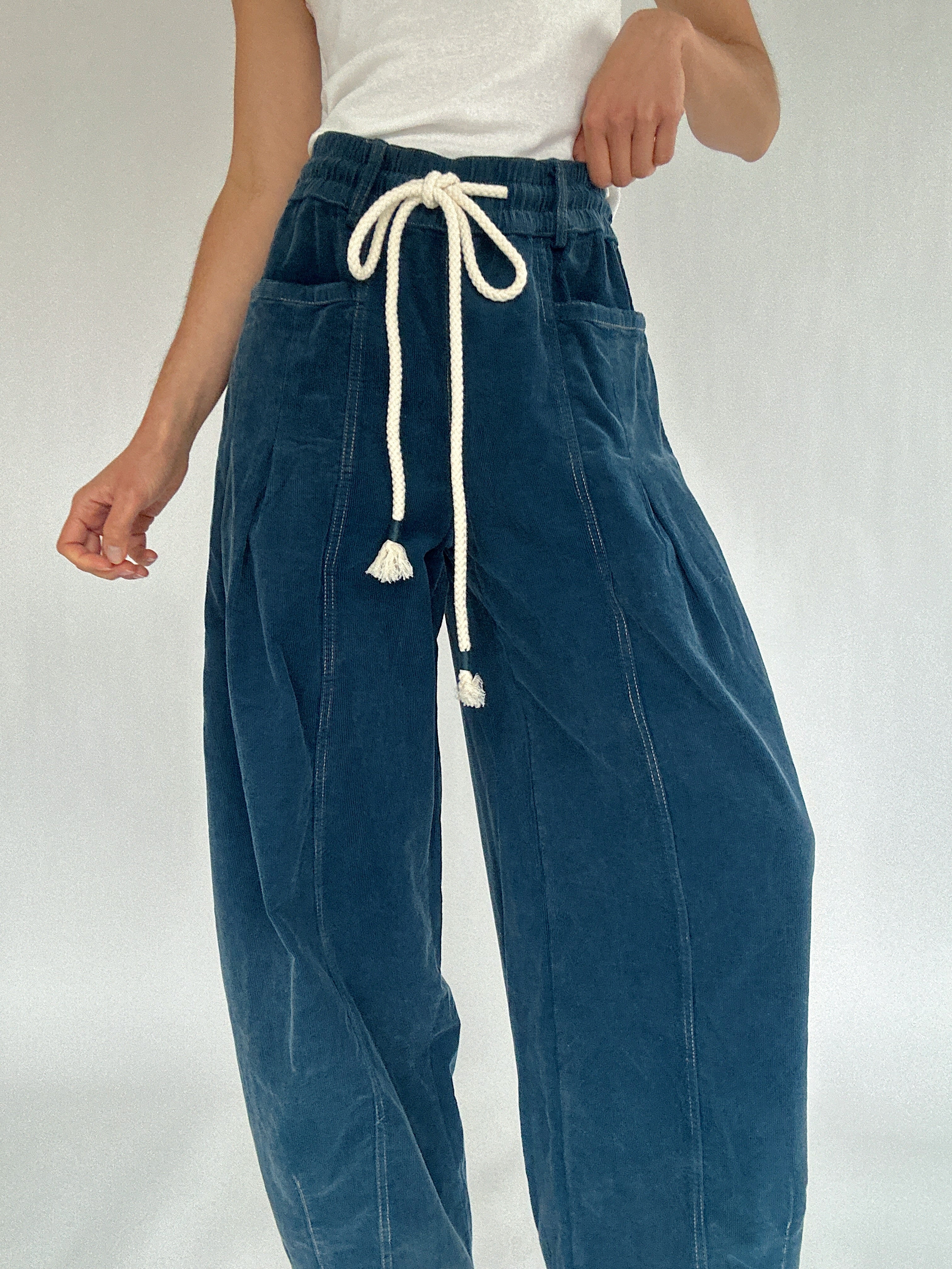 Blue corduroy pants with a white drawstring and side pockets on a plain background