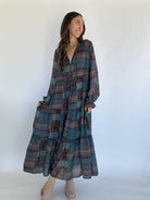 Woman wearing a pine green long, patterned dress against a white background