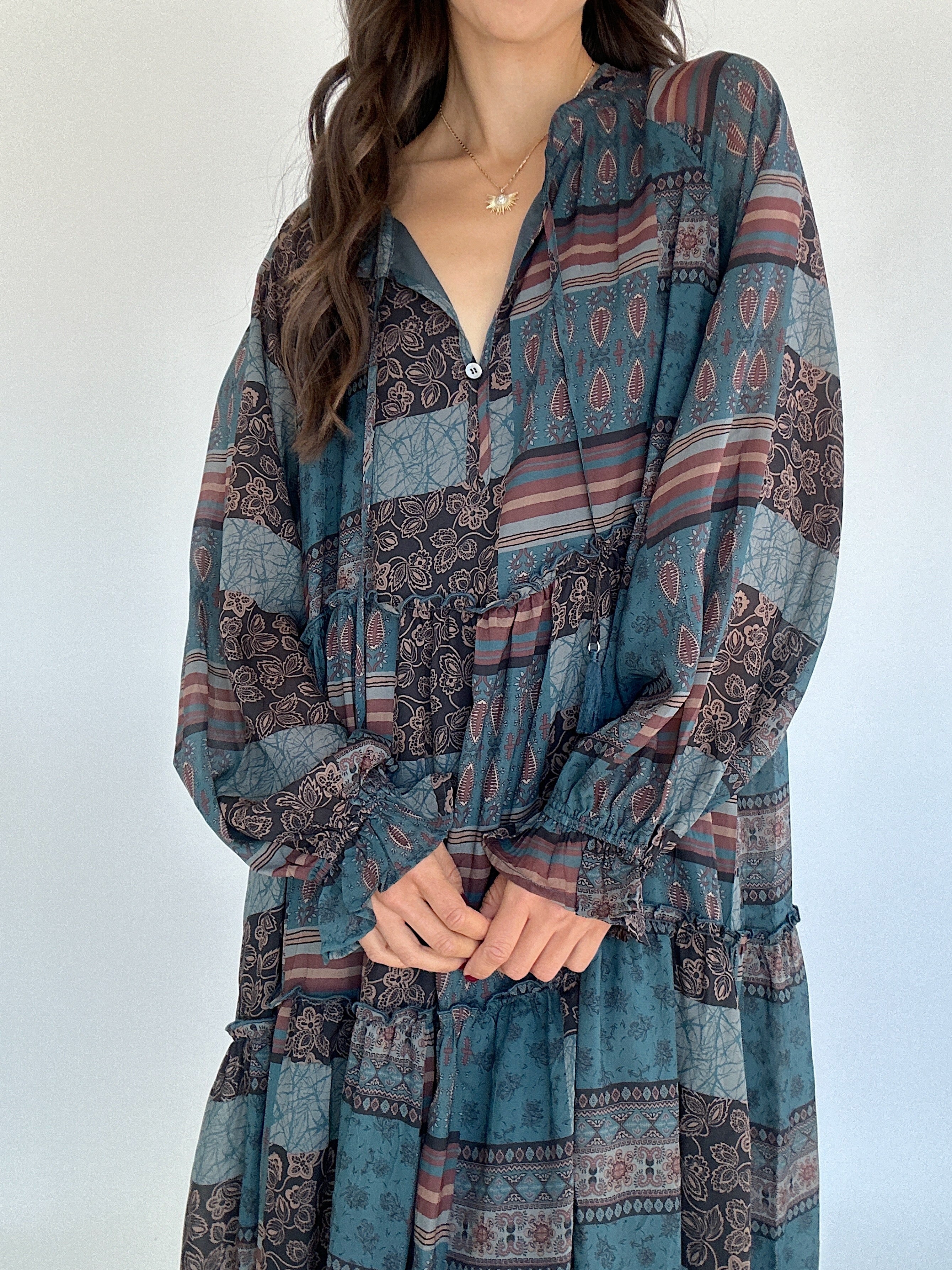 Woman wearing a long-sleeve, patterned dress against a white background showing neckline