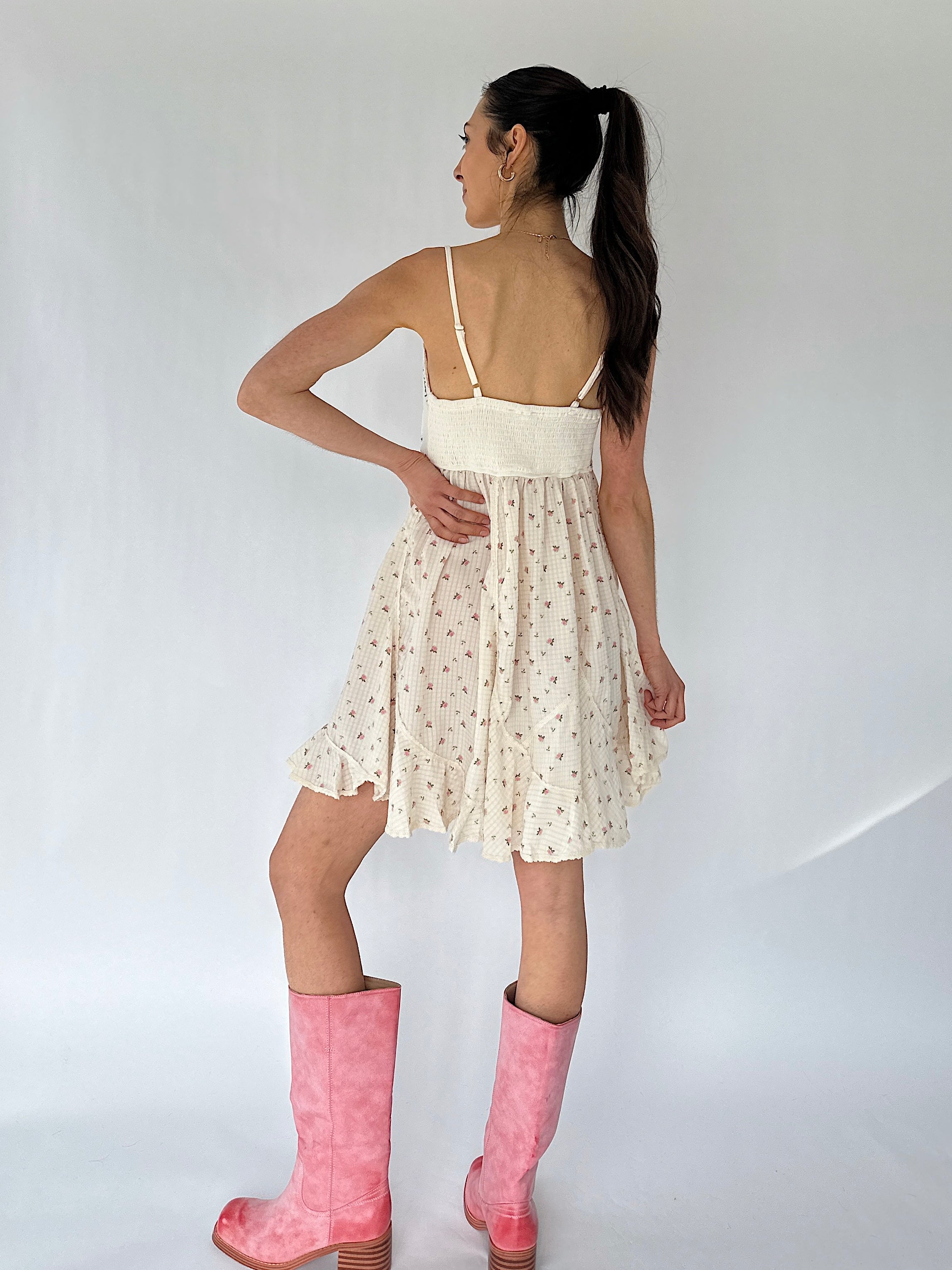 Woman wearing a white floral mini dress with pink boots on a plain background