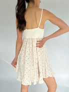 Woman wearing a white floral dress against a plain background showing smocked back