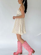 Woman wearing a white dress with small patterns and pink knee-high boots against a white background