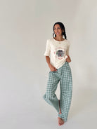 A woman modeling a cream-colored short-sleeve knit top with a graphic print and green-and-white plaid wide-leg pants, standing against a plain light gray studio background.