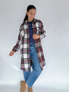 Woman wearing a long plaid jacket over a blue top and jeans on a white background