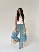 Woman wearing a white top and patchwork pants on a plain background