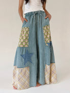Person wearing a patchwork denim wide leg pants with floral and star and plaid patches on a plain background