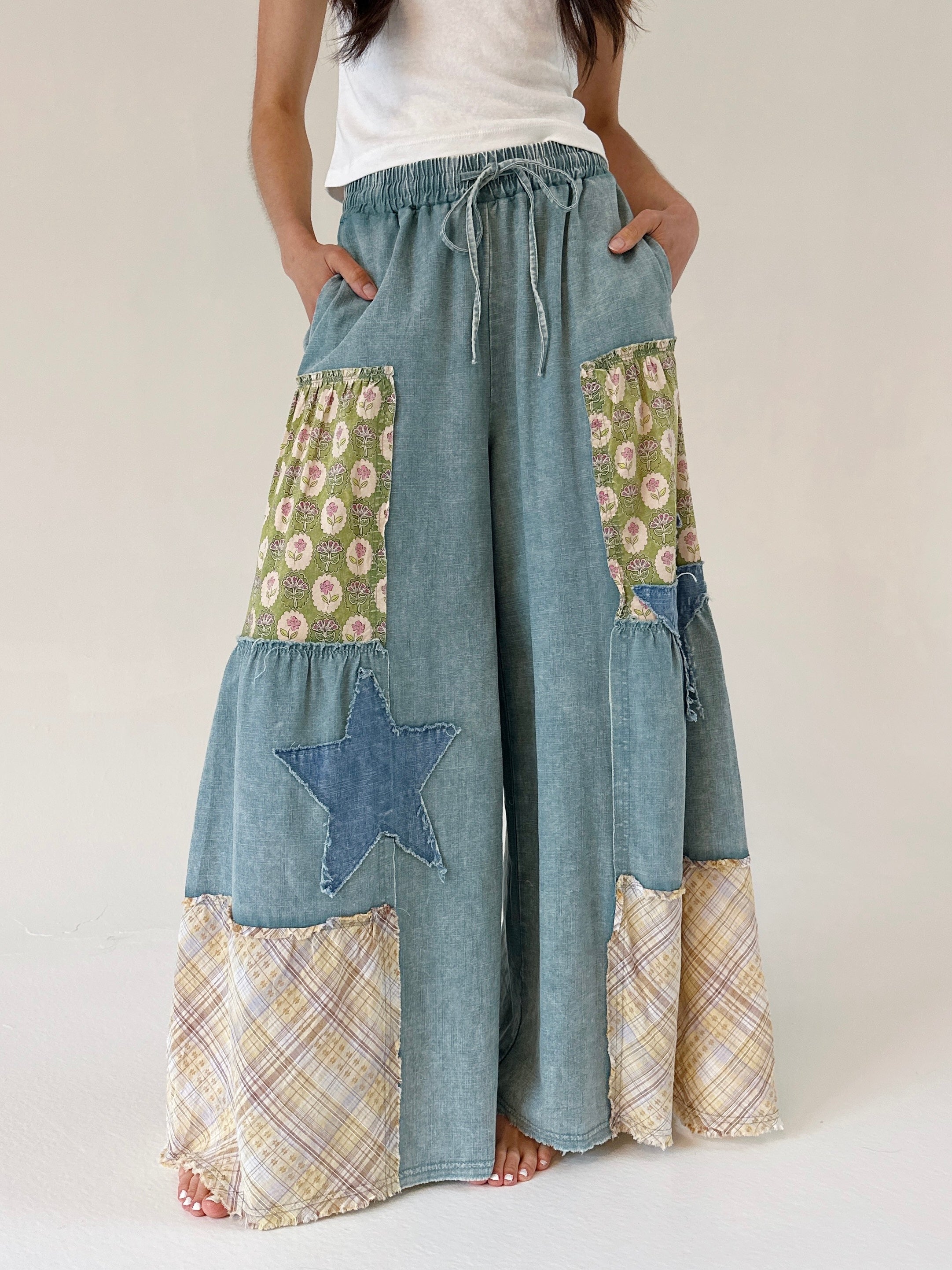 Person wearing a patchwork denim wide leg pants with floral and star and plaid patches on a plain background