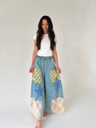 Woman wearing a white t-shirt and patchwork denim wide leg pants on a plain background
