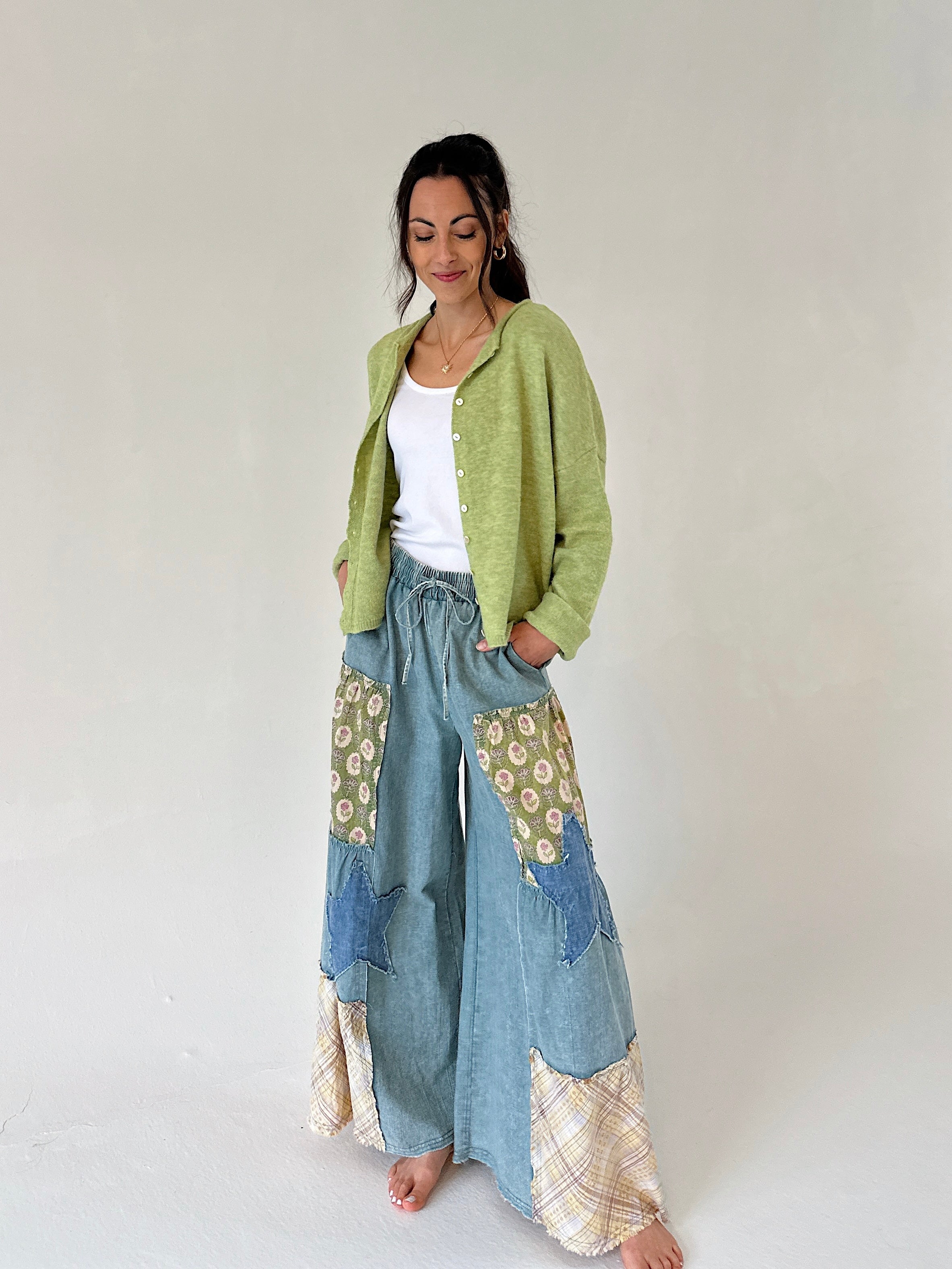 Woman wearing a green cardigan and patterned denim pants on a white background
