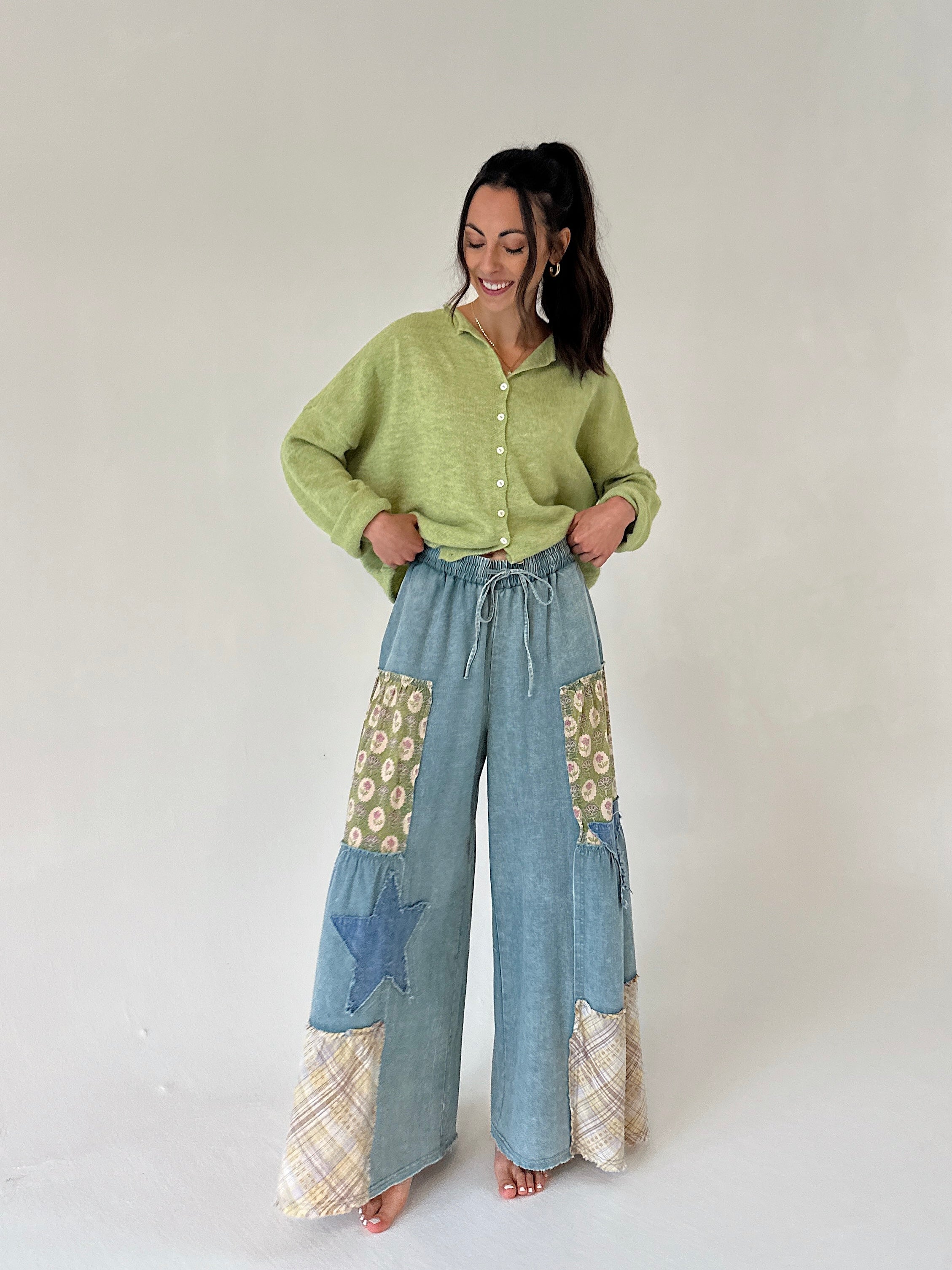 Woman wearing a green cardigan and blue patchwork pants on a white background