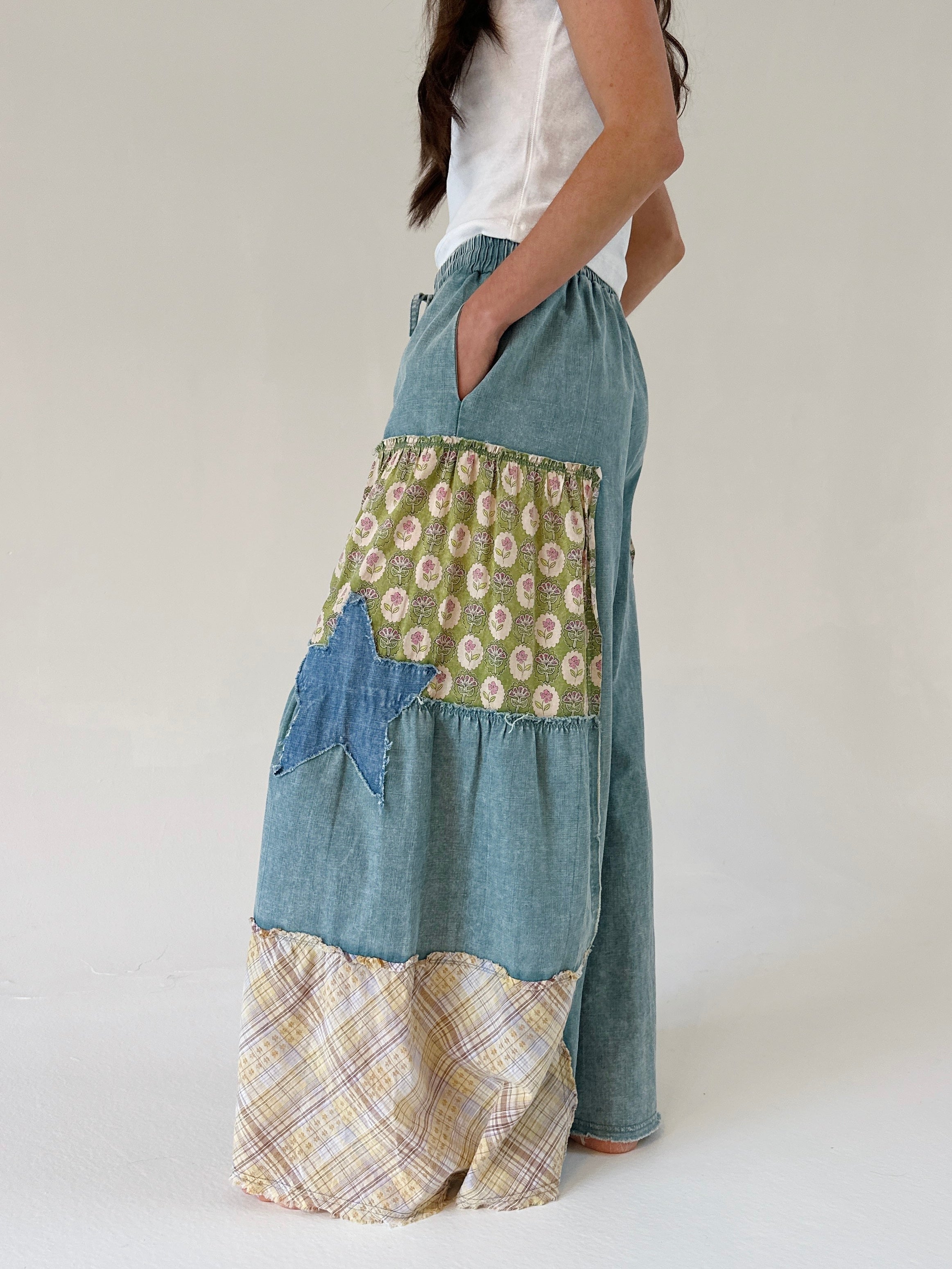 Person wearing patchwork pants with floral, plaid, and denim patterns on a white background