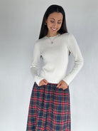 Woman wearing a white sweater and plaid skirt against a plain background