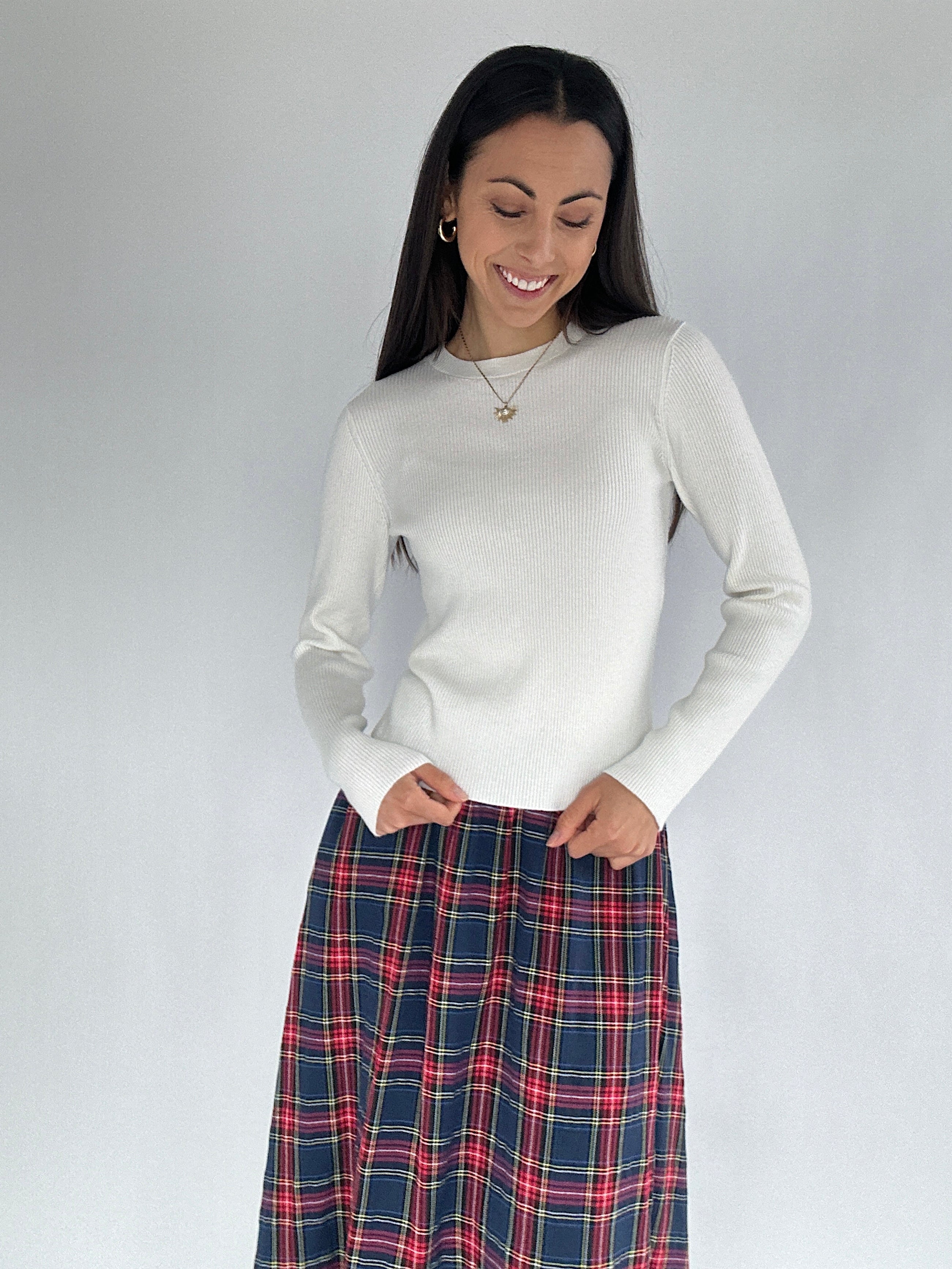 Woman wearing a white sweater and plaid skirt against a plain background