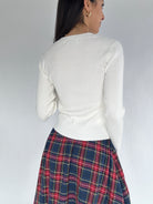Person wearing a white sweater and plaid skirt on a plain background from back