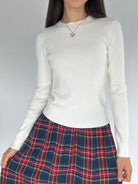 Person wearing a white long-sleeve top and a plaid skirt on a gray background