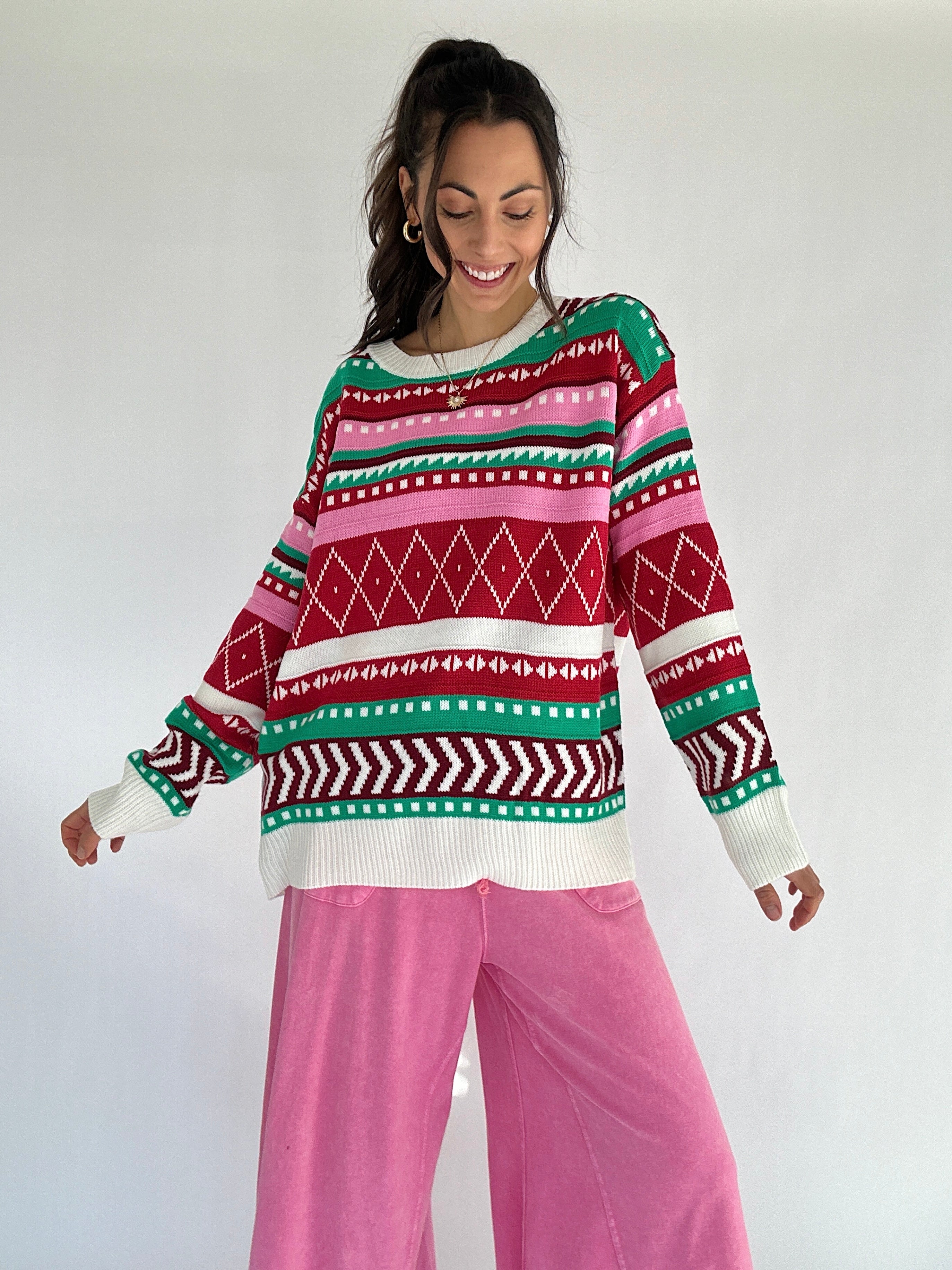 Person wearing a pink and red toned colorful patterned striped sweater and pink pants on a white background