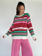 Person wearing a pink and red toned colorful patterned striped sweater and pink pants on a white background