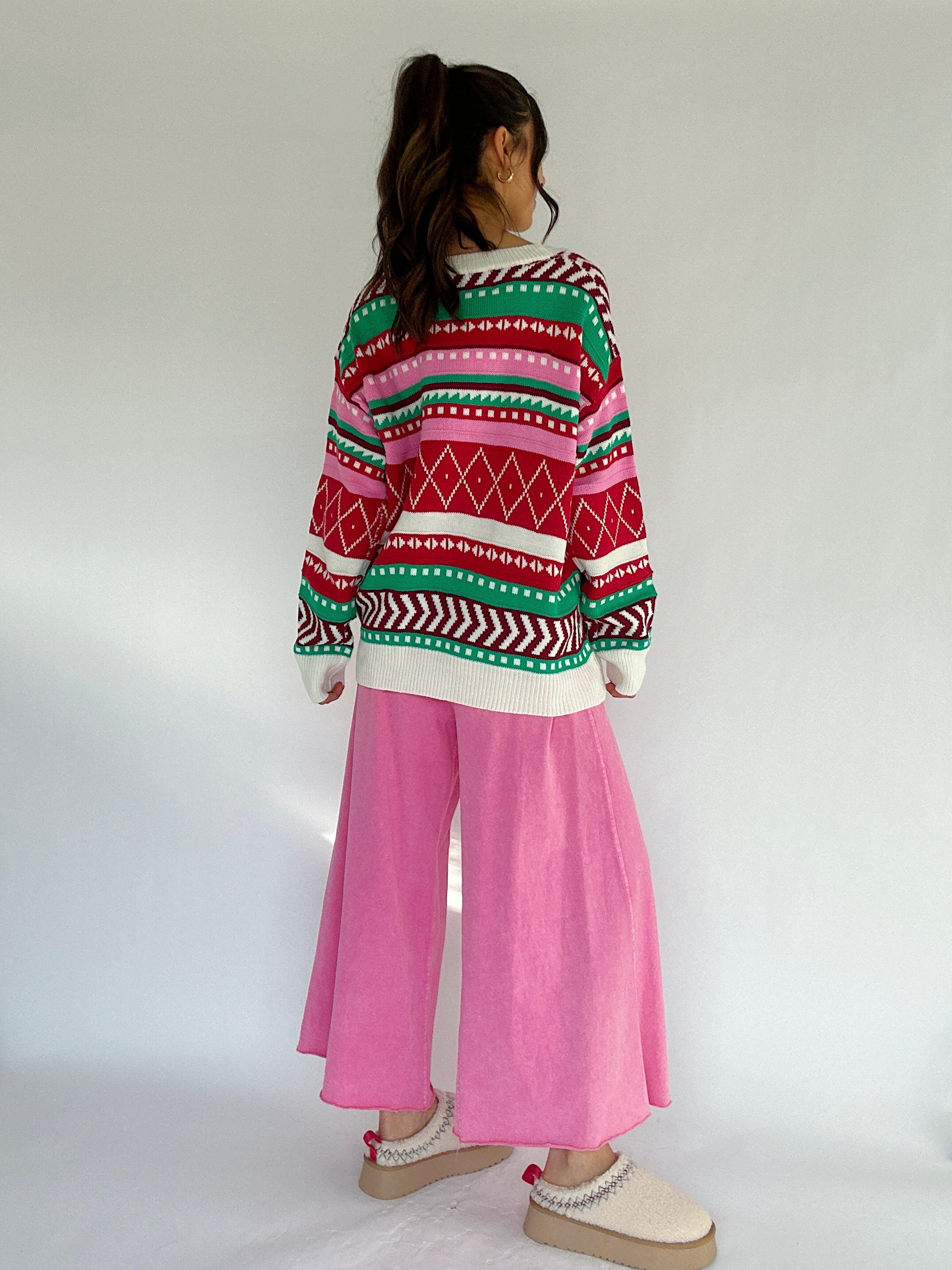 Person wearing a colorful patterned sweater and pink pants on a white background from back