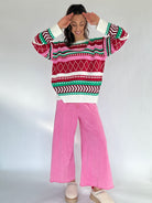 Person wearing a colorful patterned sweater and pink pants on a white background