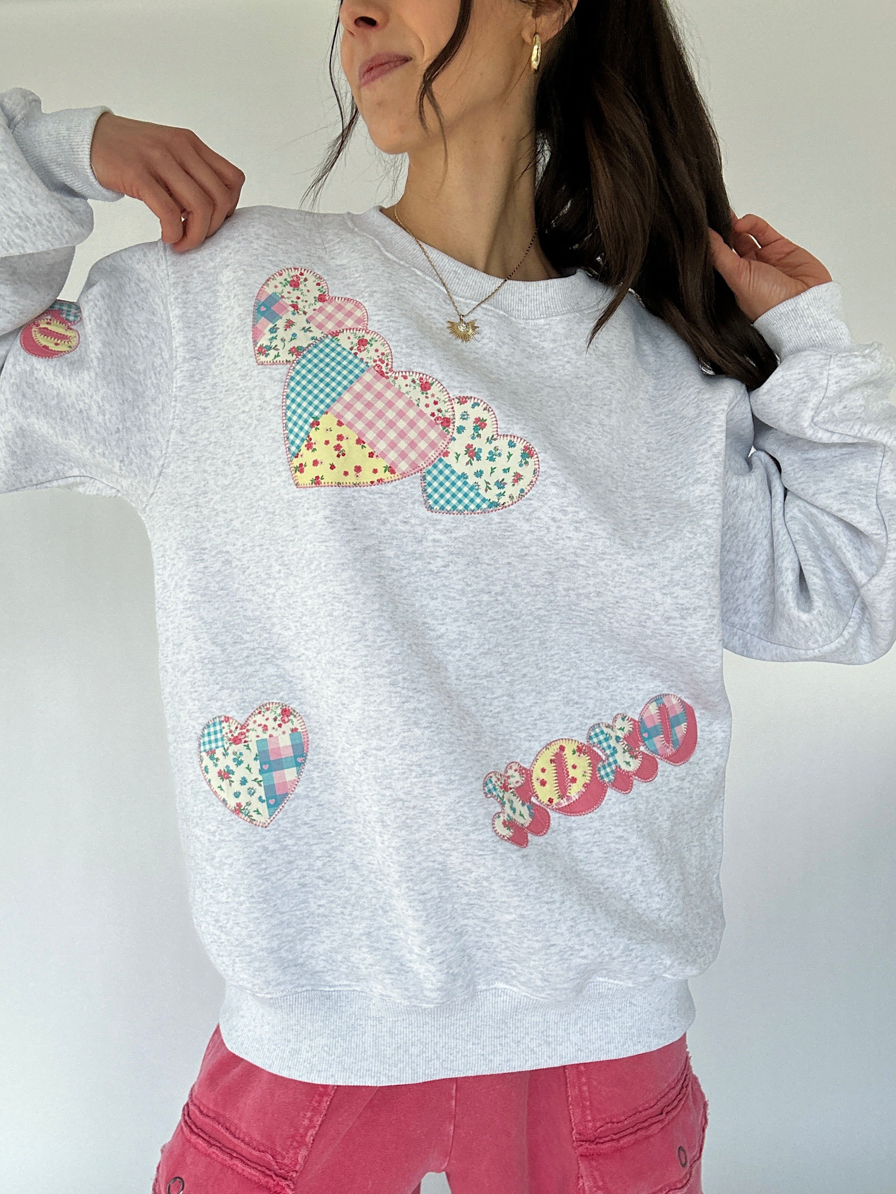 Person wearing a gray sweatshirt with colorful patch xoxo and heart designs on a white background