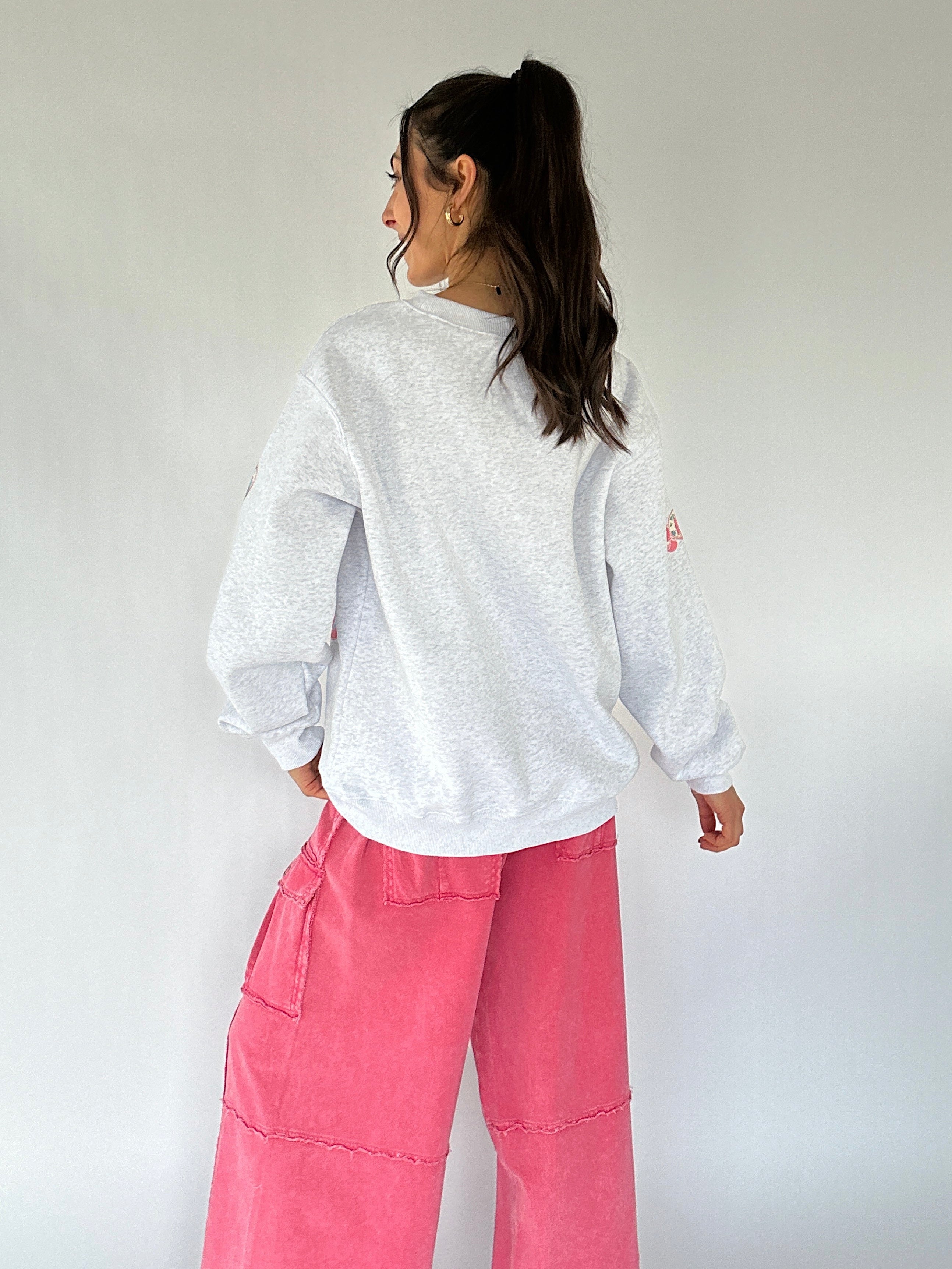 Person wearing a light gray sweatshirt and pink pants against a white background showing the back
