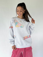 Woman wearing a gray sweatshirt with colorful patch xoxo and heart designs on a plain background