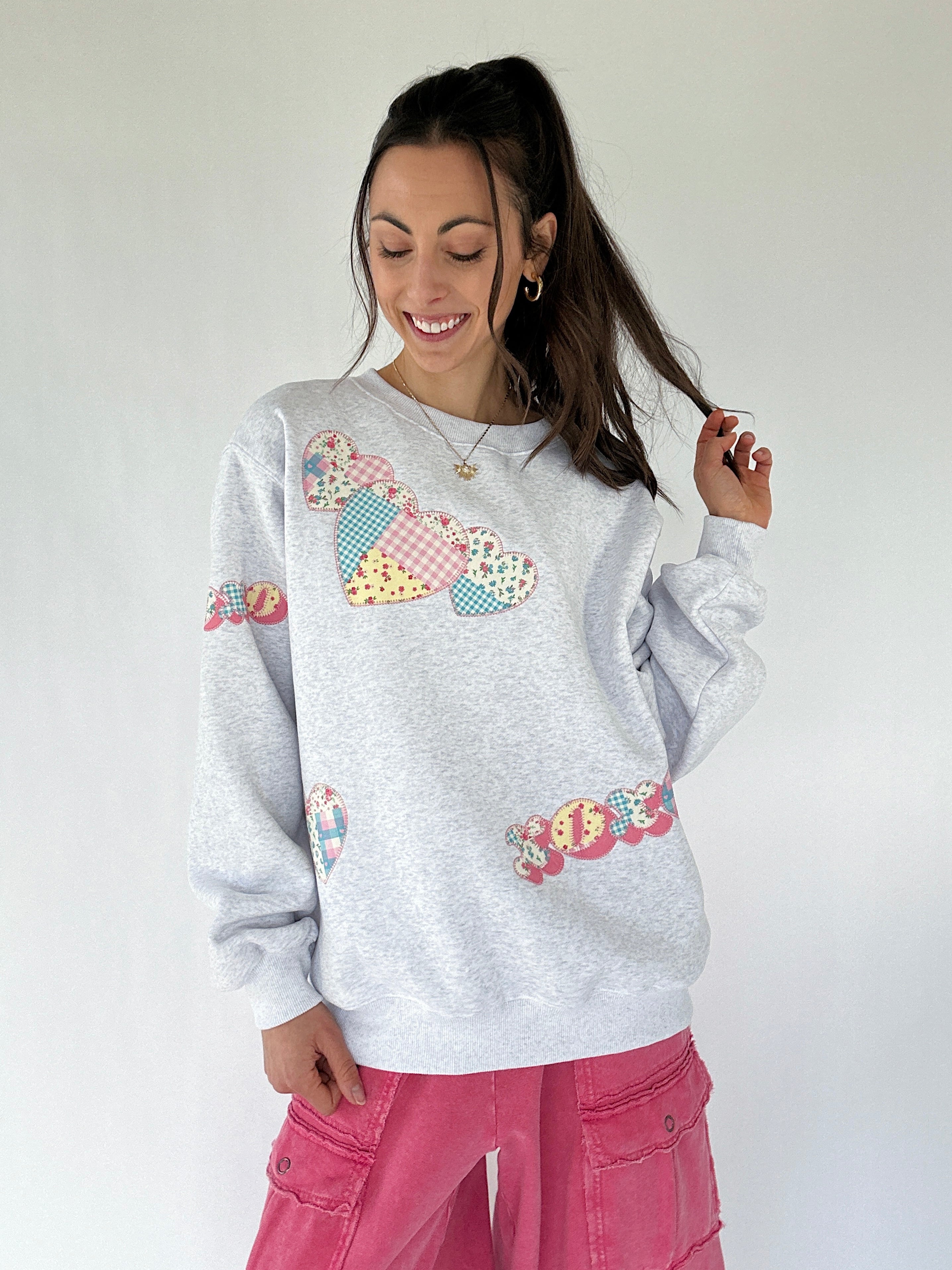 Woman wearing a gray sweatshirt with colorful patch xoxo and heart designs on a plain background