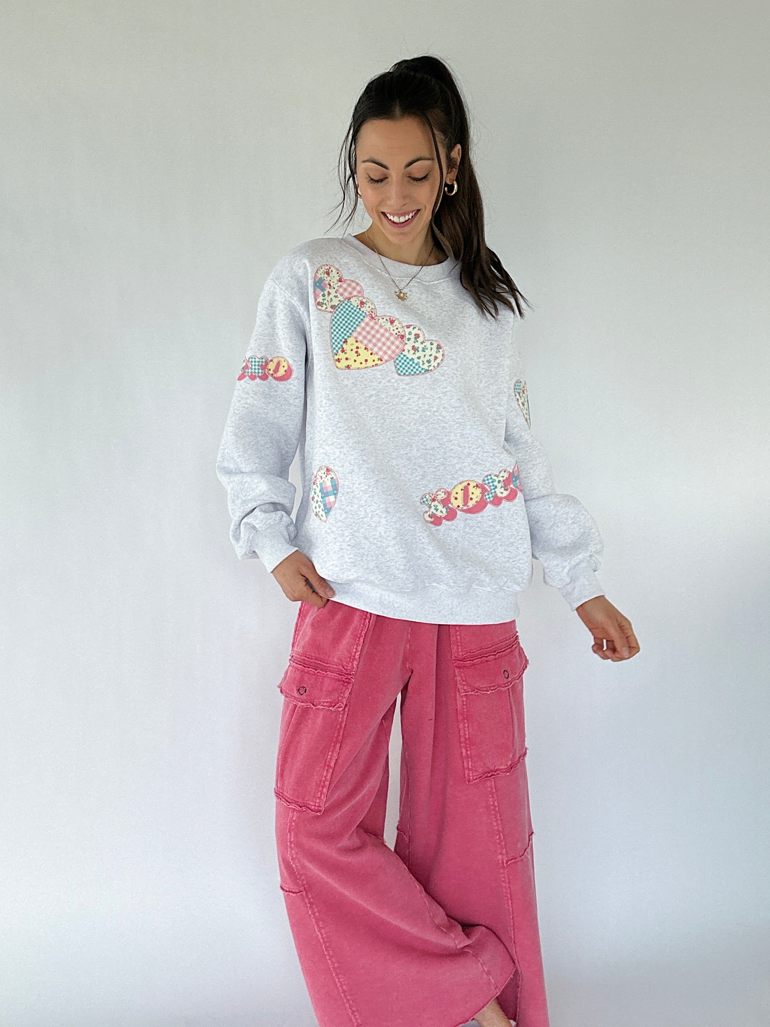 Woman wearing a gray sweatshirt with colorful patterns and pink pants against a white background