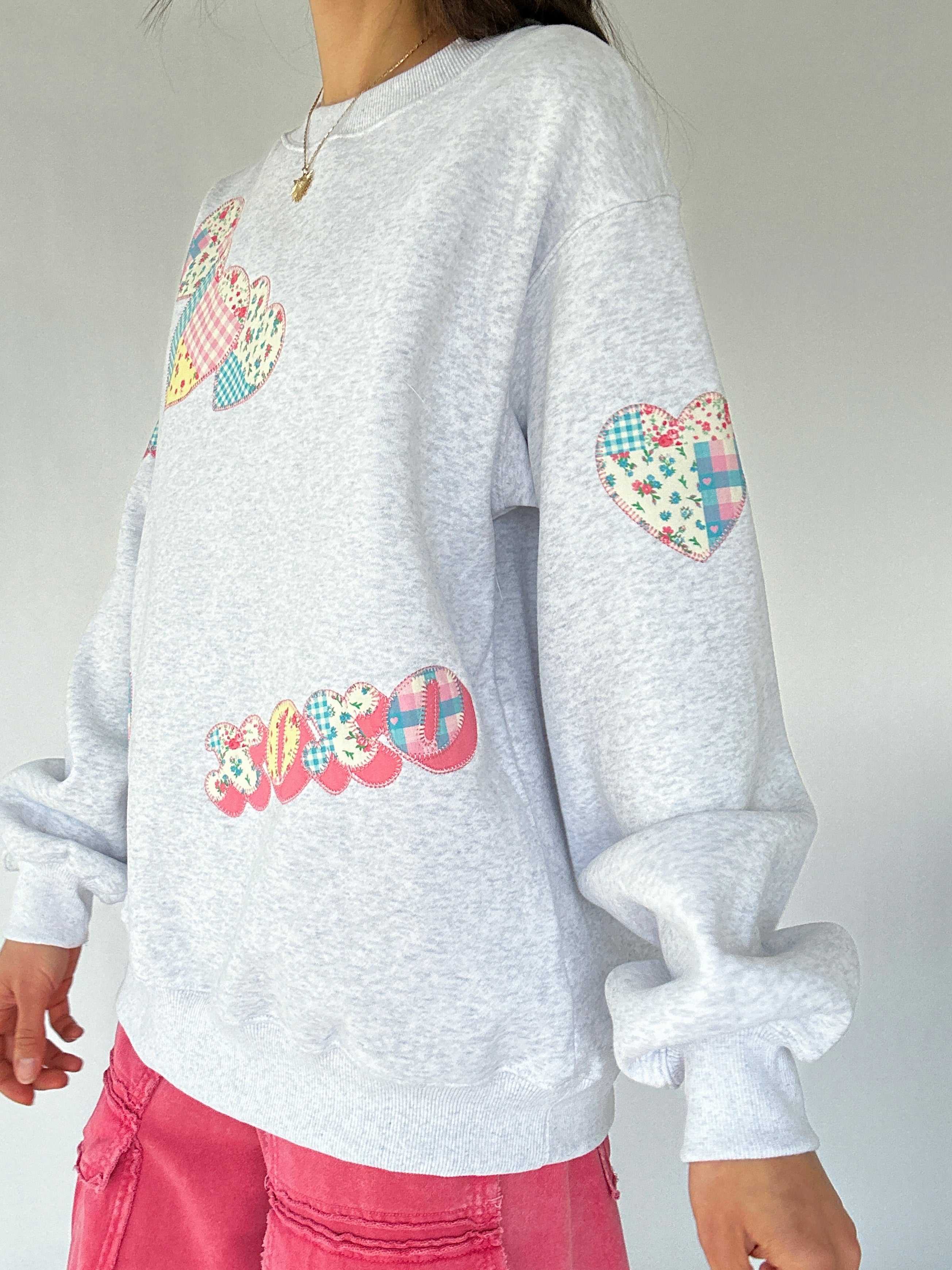 Gray sweatshirt with colorful heart and xoxo patches on a plain background