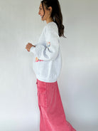 Woman wearing a gray sweatshirt with colorful designs and pink pants against a white background showing the side